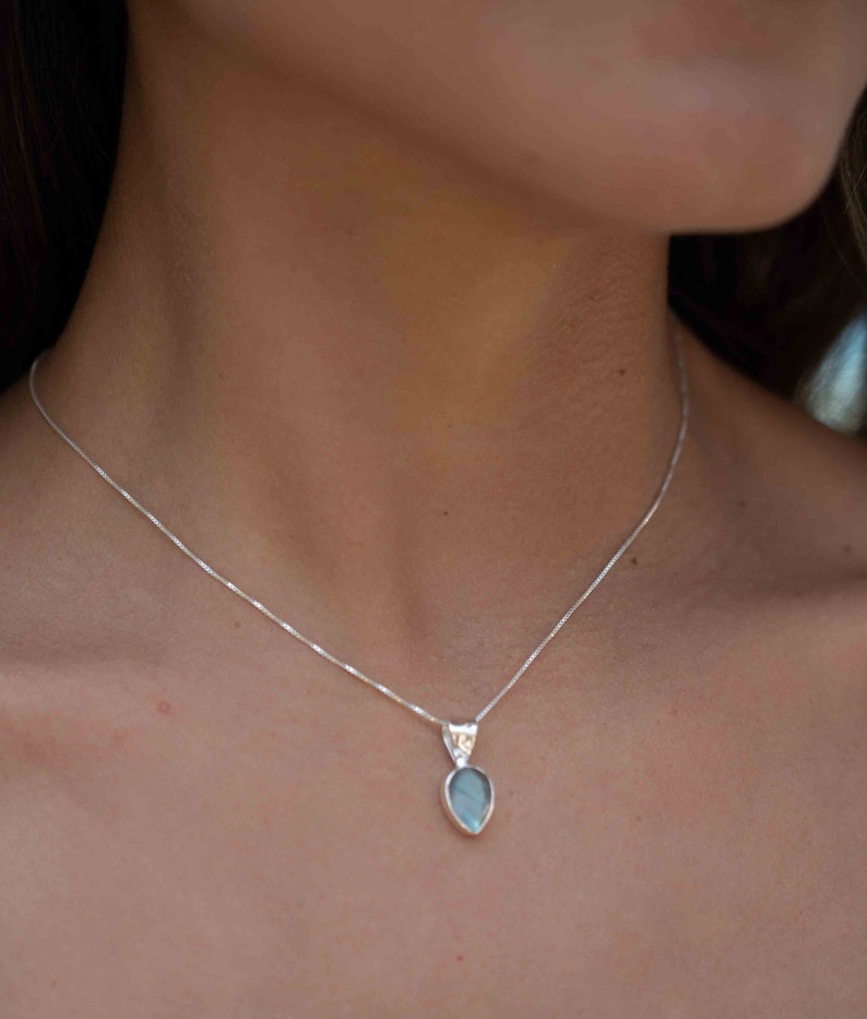May include: A silver chain necklace with a teardrop-shaped pendant featuring a blue-green gemstone.