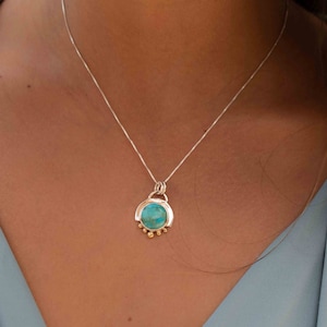 May include: A silver chain necklace with a turquoise stone pendant. The pendant is set in a silver frame with gold accents.