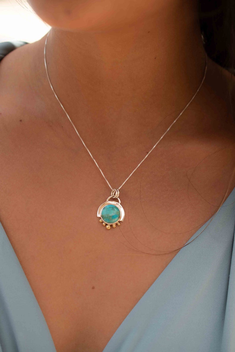 May include: A silver chain necklace with a turquoise stone pendant. The pendant is set in a silver frame with gold accents.