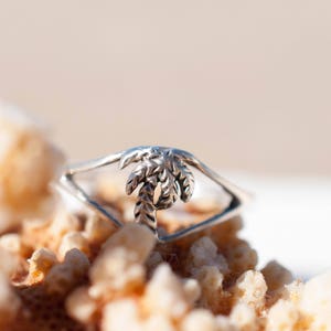 May include: A silver ring with a palm tree design. The ring is sitting on a piece of coral.
