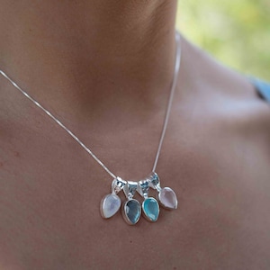 May include: A silver chain necklace with five teardrop-shaped gemstone pendants. The pendants are in shades of pink, blue, and white.