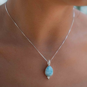 May include: A silver chain necklace with a teardrop-shaped pendant featuring a blue and white gemstone.