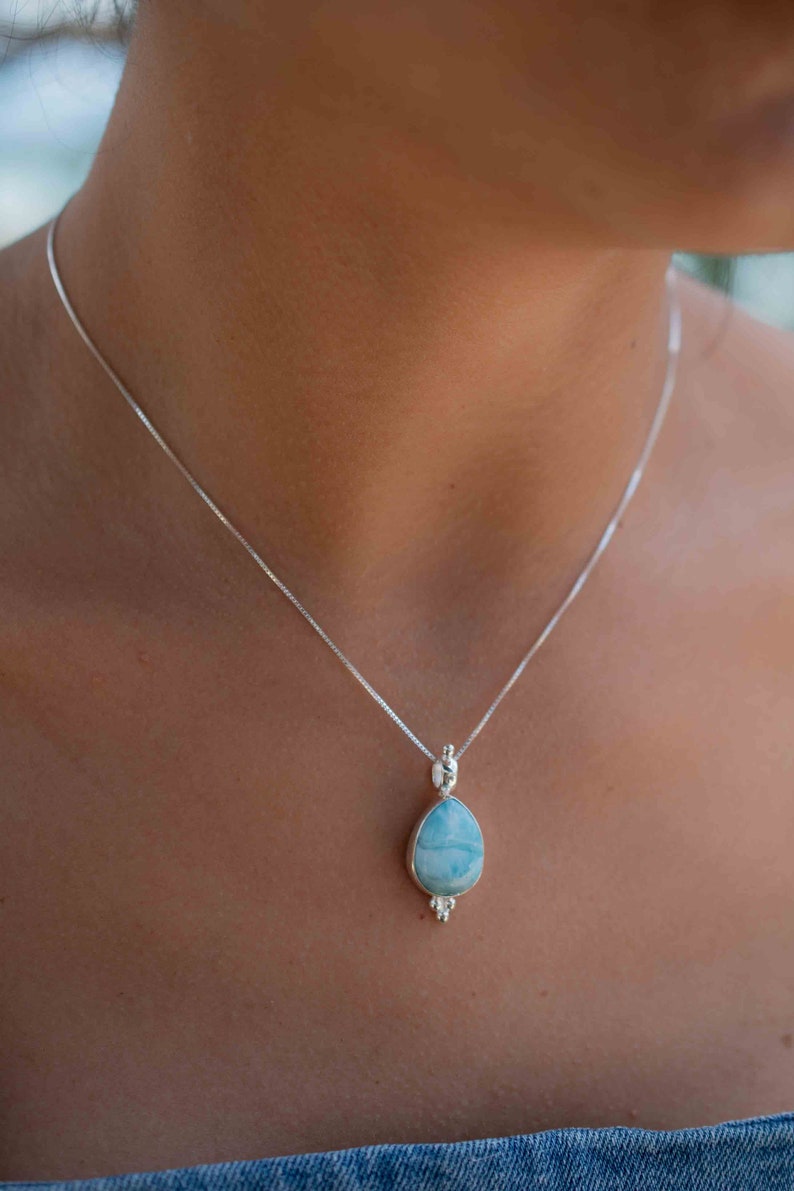 May include: A silver chain necklace with a teardrop-shaped pendant featuring a blue and white gemstone.