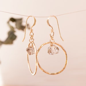 May include: Gold hoop earrings with a clear quartz crystal dangling from each hoop.