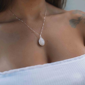 May include: A silver chain necklace with a teardrop-shaped white gemstone pendant.