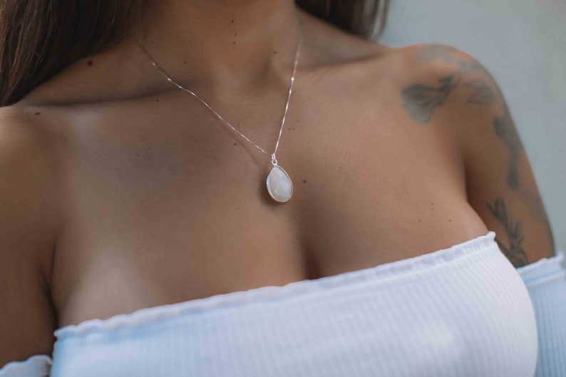 May include: A silver chain necklace with a teardrop-shaped white gemstone pendant.