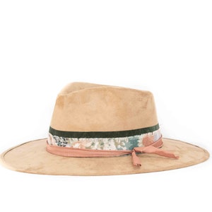 May include: A tan-colored fedora hat with a wide brim. The hat features a decorative band with floral patterns in shades of pink, blue, and green, accented by a dark green stripe and a pink ribbon tied on the side.