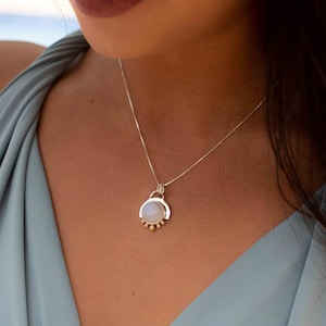 May include: A silver chain necklace with a moonstone pendant. The pendant is surrounded by a silver arch and gold beads.