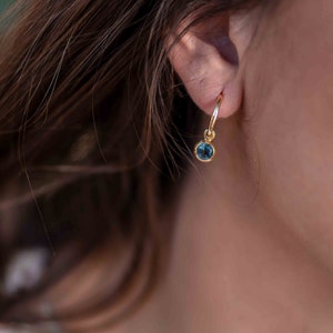 May include: A gold hoop earring with a small blue gemstone dangling from it.
