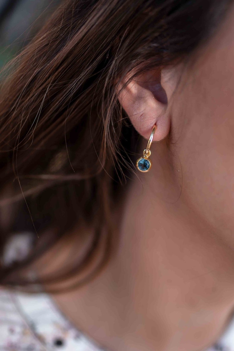 May include: A gold hoop earring with a small blue gemstone dangling from it.