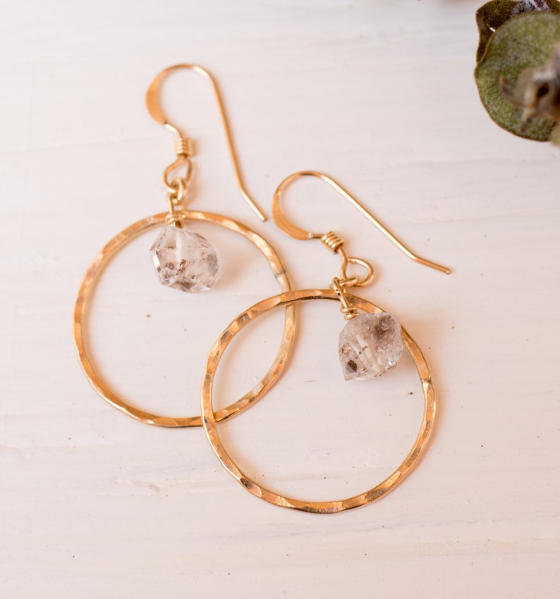 May include: Gold hoop earrings with a hammered finish and a clear quartz crystal dangling from each hoop.