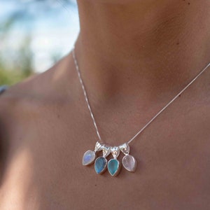 May include: A silver necklace with five teardrop-shaped pendants. The pendants are made of different gemstones, including moonstone, labradorite, aquamarine, and rose quartz.
