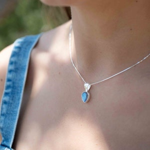 May include: A silver chain necklace with a teardrop-shaped pendant featuring a blue gemstone.