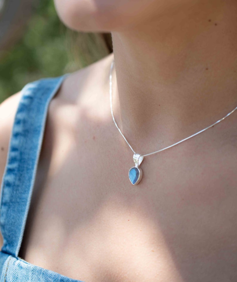 May include: A silver chain necklace with a teardrop-shaped pendant featuring a blue gemstone.