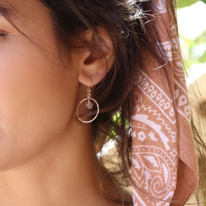 May include: A pair of gold hoop earrings with a small clear crystal charm hanging from each hoop.