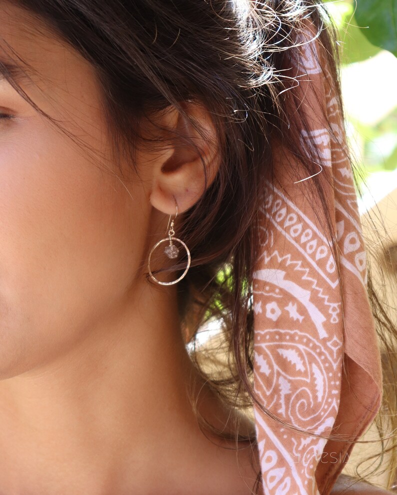 May include: A pair of gold hoop earrings with a small clear crystal charm hanging from each hoop.