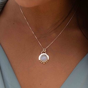 May include: A silver chain necklace with a round pendant featuring a light blue stone surrounded by a silver frame and gold accents.