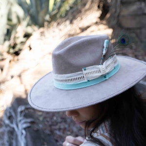 May include: A gray felt fedora hat with a light blue and white ribbon band and a peacock feather accent.