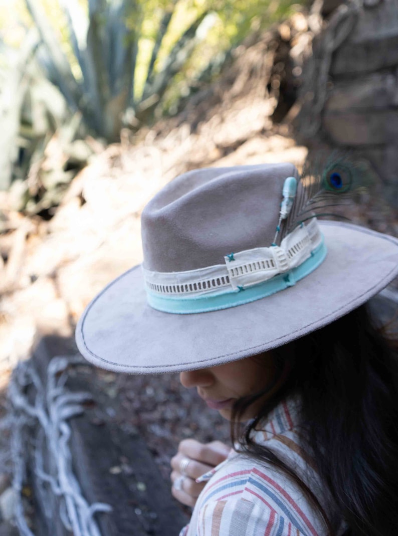 May include: A gray felt fedora hat with a light blue and white ribbon band and a peacock feather accent.