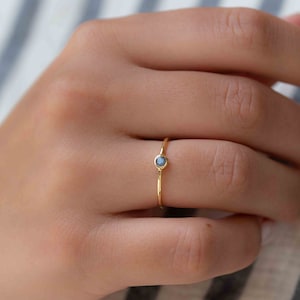 May include: A delicate gold ring with a small, round, blue gemstone.