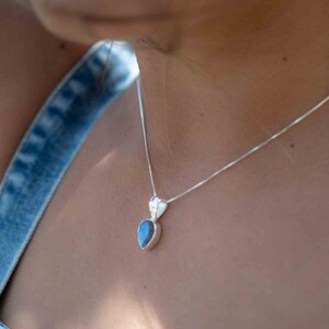 May include: A silver chain necklace with a teardrop-shaped pendant featuring a dark blue gemstone.