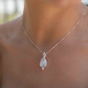 May include: A silver chain necklace with a teardrop-shaped pendant featuring a white moonstone.
