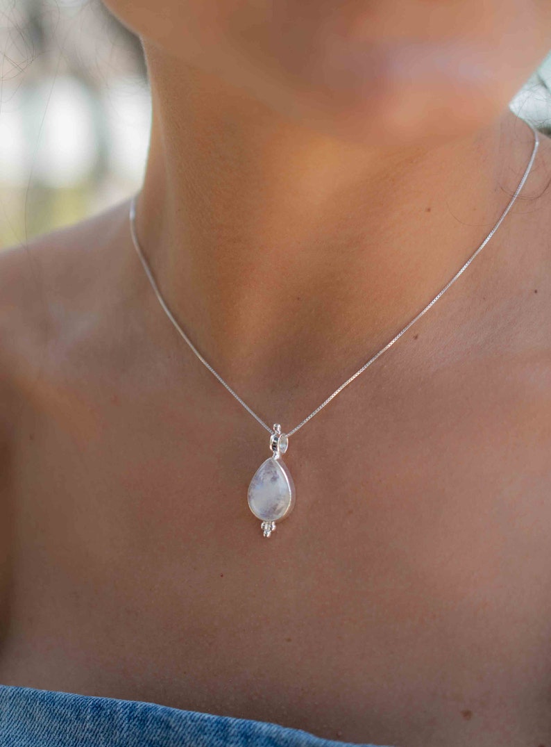 May include: A silver chain necklace with a teardrop-shaped pendant featuring a white moonstone.