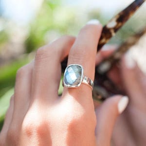 May include: A silver ring with a large, rectangular, iridescent gemstone. The gemstone has a faceted cut and is set in a simple band.