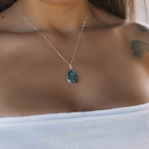 May include: A silver chain necklace with a teardrop-shaped pendant featuring a blue and green gemstone.