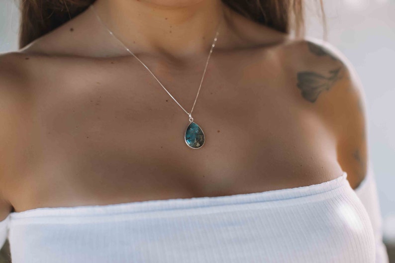 May include: A silver chain necklace with a teardrop-shaped pendant featuring a blue and green gemstone.
