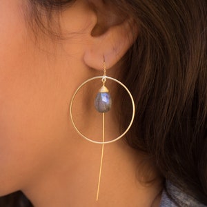 May include: Gold hoop earrings with a dangling, teardrop-shaped, iridescent blue gemstone.