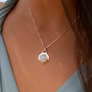 May include: A silver chain necklace with a moonstone pendant. The pendant is surrounded by a silver frame and has small gold beads around the bottom.
