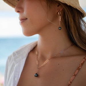 K&ouml;nnte beinhalten: Eine Frau tr&auml;gt einen Strohhut und ein wei&szlig;es Hemd mit einer goldenen Kettenkette und Ohrringen mit einem schwarzen Perlenanh&auml;nger. Die Kette und die Ohrringe sind von der Marke "Mares&iacute;a Jewelry".