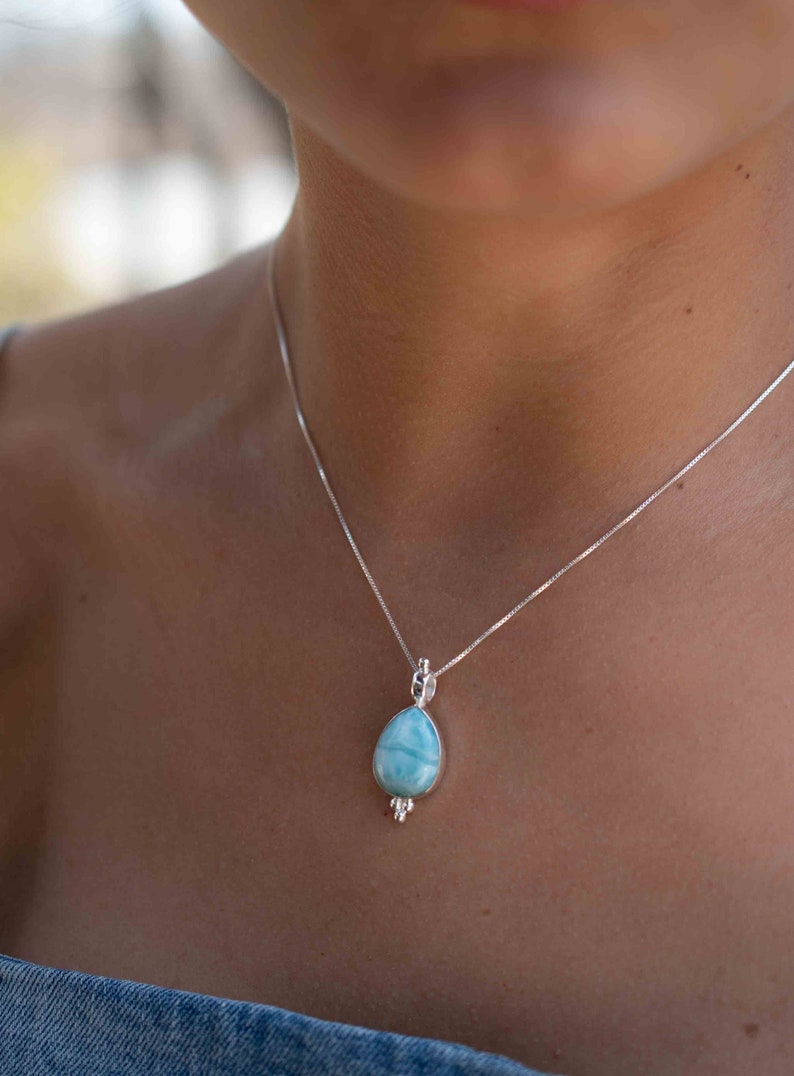 May include: A silver chain necklace with a teardrop-shaped blue gemstone pendant.
