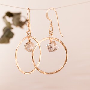 May include: Gold hoop earrings with a clear crystal dangling from each hoop.