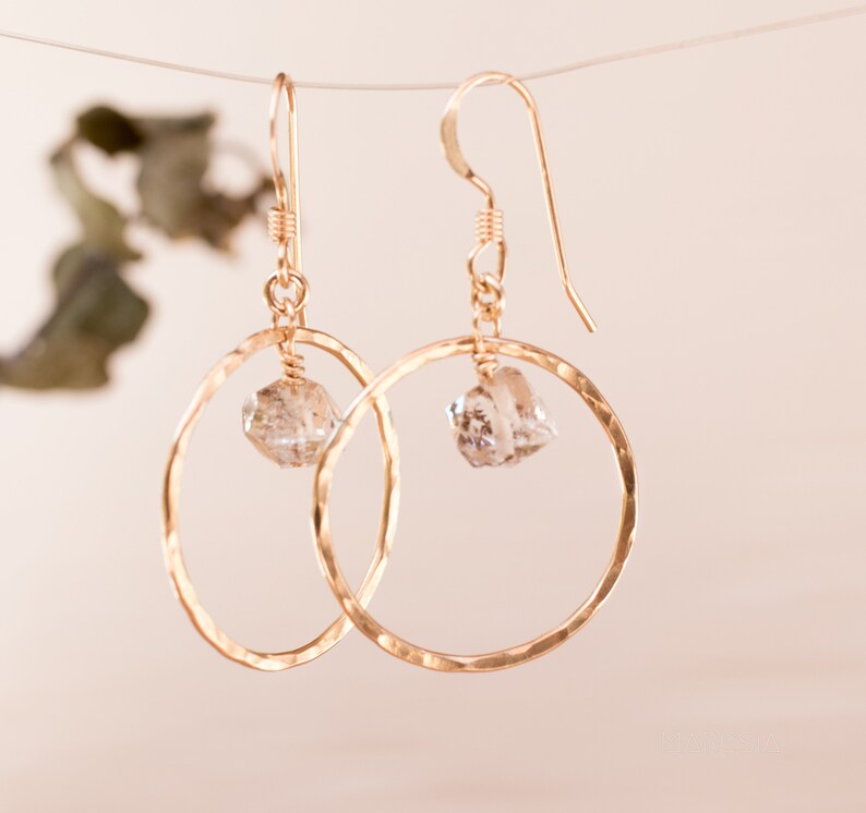 May include: Gold hoop earrings with a clear crystal dangling from each hoop.