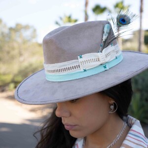May include: A gray suede hat with a white and light blue ribbon and a turquoise and peacock feather accent.