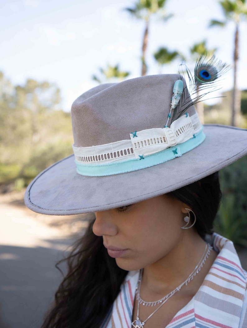 May include: A gray suede hat with a white and light blue ribbon and a turquoise and peacock feather accent.