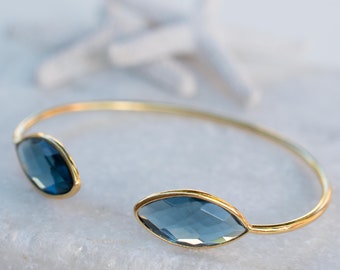 May include: A gold bangle bracelet with two large, faceted, oval-shaped blue gemstones.