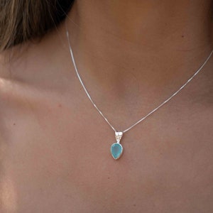 May include: A silver chain necklace with a light blue teardrop-shaped pendant.