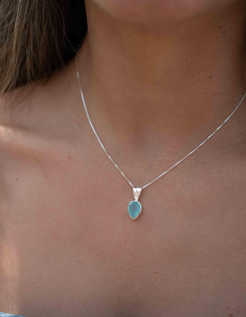 May include: A silver chain necklace with a light blue teardrop-shaped pendant.