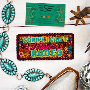 May include: An assortment of Western-themed accessories, including a belt with turquoise-colored stones, a patch with the text "SORRY, I CAN'T have a RODEO", and a business card. The patch has a floral design and the text is in turquoise.