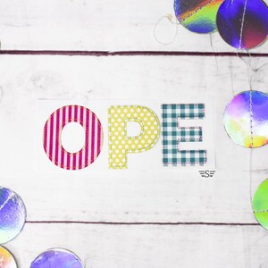 May include: A white rectangular sign with the word "OPEN" in colorful, patterned letters. The "O" has pink and white vertical stripes, the "P" is yellow with white polka dots, and the "E" is blue and white checkered. Iridescent circles are scattered around the sign.
