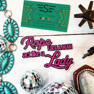 May include: Two pink and black iron-on patches with the text "Rope like a man act like a Lady".