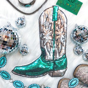 May include: A turquoise and silver sequined cowboy boot applique with a white star design. The boot is surrounded by silver disco balls, a turquoise and silver beaded belt, and a silver bracelet.