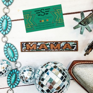 May include: A brown and tan embroidered patch with the word "MAMA" in large, orange letters on a camouflage background.