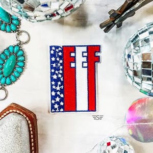 May include: A red, white, and blue embroidered patch with the word "EFF" in white letters. The patch is in the shape of a rectangle and has a star-spangled design on the left side.