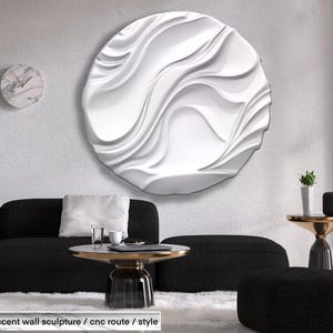May include: A white, circular wall sculpture with a flowing, wave-like design. The sculpture is mounted on a textured white wall above a black sofa and a round coffee table. A marble clock and a small side table are also visible.