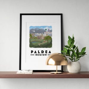 May include: A framed art print featuring a watercolor illustration of the Paldea Region, with the text "PALDEA REGION" below the image. The print is displayed on a wooden shelf with a gold lamp and a potted plant.