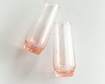 May include: Two pink glass champagne flutes with a textured surface.
